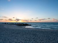 a lone bench sits on the beach as the sun sets behind clouds and water in the background