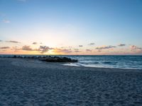 a lone bench sits on the beach as the sun sets behind clouds and water in the background