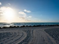 there is a large amount of footprints in the sand on the beach at sunset, and the sun shining behind the beach