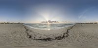 fish eye view of a sun set over the beach with people in the background and a seagull at the end of the sand