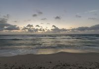 a lone surfer on a sandy beach in the ocean at sunset time, under a cloudy sky