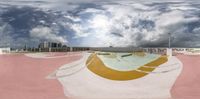 an empty skateboard ramp at a skate park with buildings in the background and clouds overhead