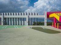 a big building with colorful railings is outside a parking lot against a cloudy blue sky