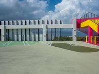 a big building with colorful railings is outside a parking lot against a cloudy blue sky