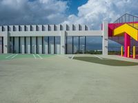 a big building with colorful railings is outside a parking lot against a cloudy blue sky