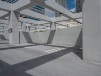 a concrete parking garage and a clear blue sky with white columns and beams above the concrete