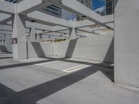 a concrete parking garage and a clear blue sky with white columns and beams above the concrete