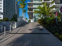 the entrance to an apartment with palms trees and bushes in the foreground, next to a concrete driveway