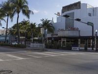 there is a white theater building on the corner of the street with palm trees near by