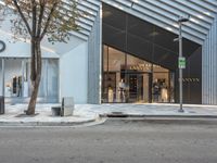 two women walking outside of a clothing store near trees and buildings with two people on bikes passing by