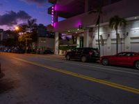 two cars parked next to each other near a hotel at dusk with a sign that says miami neon on it