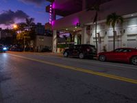 two cars parked next to each other near a hotel at dusk with a sign that says miami neon on it