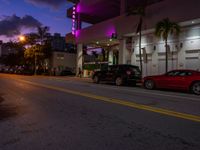 two cars parked next to each other near a hotel at dusk with a sign that says miami neon on it