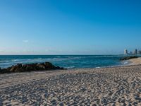 a sandy beach with the ocean and high rise buildings in the background during the day