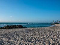 a sandy beach with the ocean and high rise buildings in the background during the day