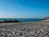 a sandy beach with the ocean and high rise buildings in the background during the day