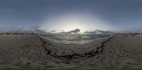 fish - eye view of the ocean from the sand in the distance with a very cloudy sky and sun