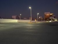 an empty parking lot next to a city building at night with streetlights in the foreground