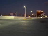 an empty parking lot next to a city building at night with streetlights in the foreground