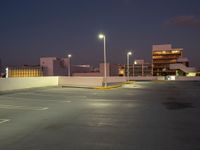 an empty parking lot next to a city building at night with streetlights in the foreground