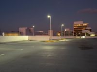 an empty parking lot next to a city building at night with streetlights in the foreground