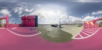 a street view through a fish eye lens of a bus terminal and parking lot on pink concrete