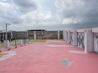 pink floor tiles on a tennis court with several lockers around it and clouds in the sky