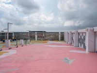 pink floor tiles on a tennis court with several lockers around it and clouds in the sky