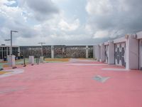 pink floor tiles on a tennis court with several lockers around it and clouds in the sky