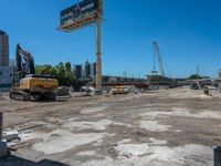 two construction vehicles in a construction site with people walking nearby in the background and under the blue sky