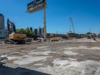 two construction vehicles in a construction site with people walking nearby in the background and under the blue sky