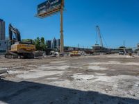 two construction vehicles in a construction site with people walking nearby in the background and under the blue sky