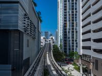 a train going down a tracks between tall buildings and a blue sky background behind it