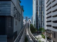 a train going down a tracks between tall buildings and a blue sky background behind it