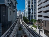 a train going down a tracks between tall buildings and a blue sky background behind it