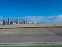 a highway with two lanes and no parking on it with a city skyline in the background