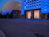 an empty road with blue lights on the building behind it in a dark night sky