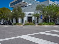 a big building with trees, grass and plants by a road way and people walking down the sidewalk