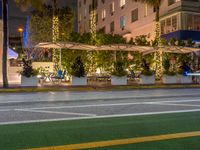 a restaurant in the middle of an urban road at night in the city, with people seated beneath the awnings and trees