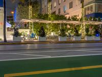 a restaurant in the middle of an urban road at night in the city, with people seated beneath the awnings and trees