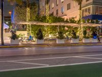 a restaurant in the middle of an urban road at night in the city, with people seated beneath the awnings and trees