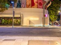 two people walking on the sidewalk by some buildings at night in the city, with red light to the right