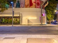 two people walking on the sidewalk by some buildings at night in the city, with red light to the right