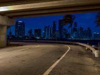 the city skyline is seen from underneath a freeway with yellow lines on it, while buildings lit up in blue