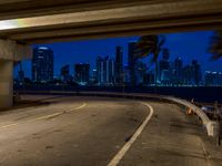 the city skyline is seen from underneath a freeway with yellow lines on it, while buildings lit up in blue