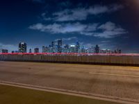 an empty highway with city skyline behind it at night time, lit up by red lights