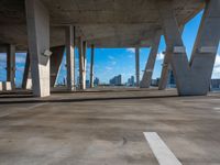 an empty concrete parking lot with many columns and columns holding it together in view of a city skyline