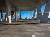 an empty concrete parking lot with many columns and columns holding it together in view of a city skyline