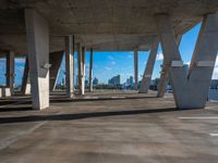 an empty concrete parking lot with many columns and columns holding it together in view of a city skyline