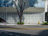 a yellow fire hydrant is in a city street by a building that has white lattices over it